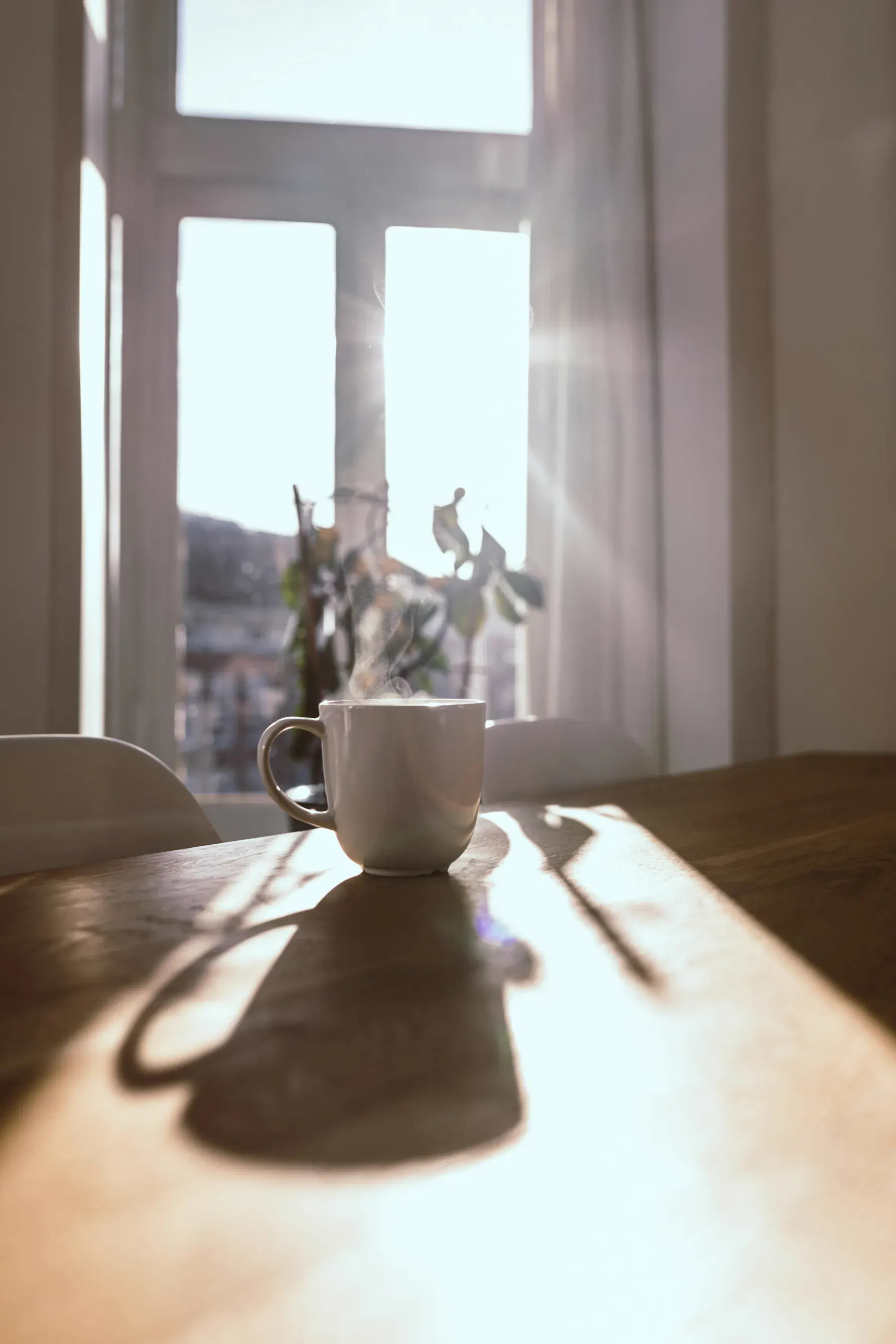 Xícara de café fumegante sobre uma mesa de madeira, com luz da manhã entrando por uma janela